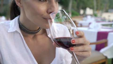 Young, happy woman tasting red wine sitting in beach restaurant 
