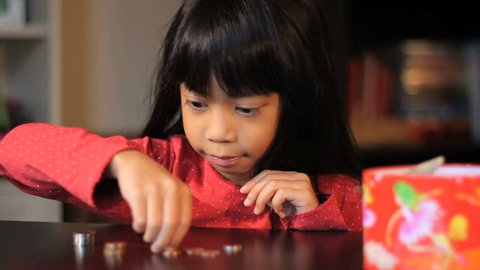A cute little six year old Asian girl counts up her money.