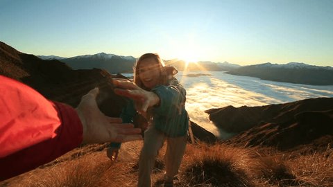 Teammate helping hiker to reach summit .
Couple hiking in New Zealand, hand reach out to help female hiker reach the summit.
A helping hand concept 