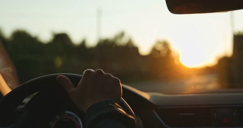 Man Driving a Car at Sunset. SLOW MOTION 4K DCi. Male Hand on steering wheel close up. Beautiful Road in blurred background.