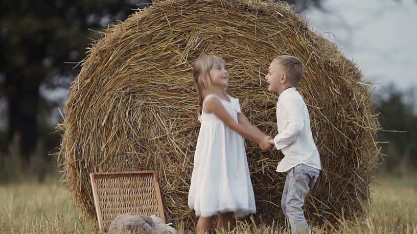 Two young children have fun jumping in the field. Boy and girl eat fruit. Sunset slow motion