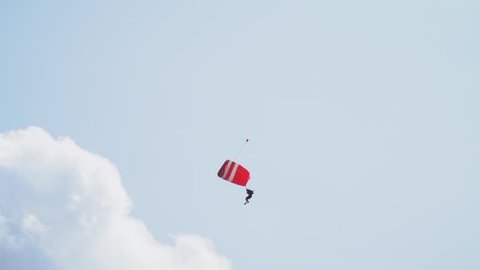A paratrooper with a red sports parachute quickly flies down and lands in front of a crowd of spectators
