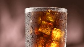 Cola with ice cubes background. Cola drink with Ice and bubbles and water drops on glass. Soda closeup. Food background. Rotation Fizzy drink. 4K UHD video footage. Ultra high definition 3840X2160