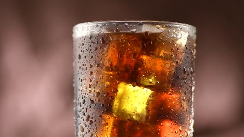 Cola with ice cubes background. Cola drink with Ice and bubbles and water drops on glass. Soda closeup. Food background. Rotation Fizzy drink. 4K UHD video footage. Ultra high definition 3840X2160