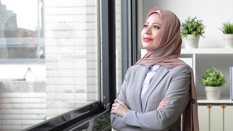 young professional muslim business woman walking to window and looking at outside thinking work plan.