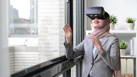happy pretty muslim business woman using virtual reality goggles watching company case plan and touching simulation screen to move document.