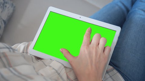 Young Woman in blue jeans laying on bed uses Tablet PC with pre-keyed green screen. Few types of gestures - scrolling up and down, tapping, zoom in and out. Perfect for screen compositing
