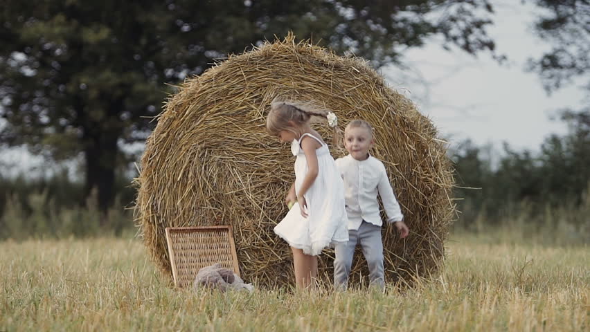 Two young children have fun jumping in the field. Boy and girl eat fruit. Sunset slow motion