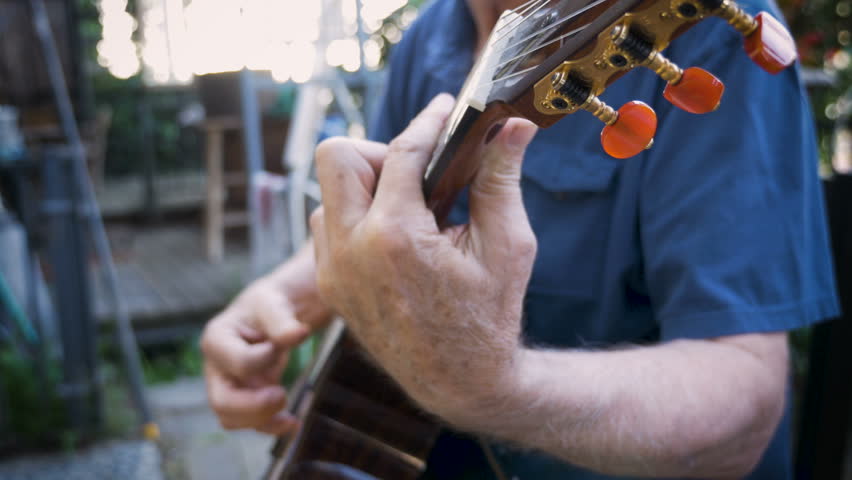 Healthy handsome retired baby boomer senior man finger picking and playing music on his acoustic guitar outside tilt up