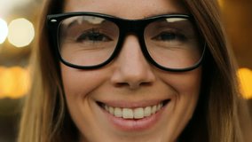 Close up portrait shot of young woman in glasses looking at the camera and smiling outdoors.