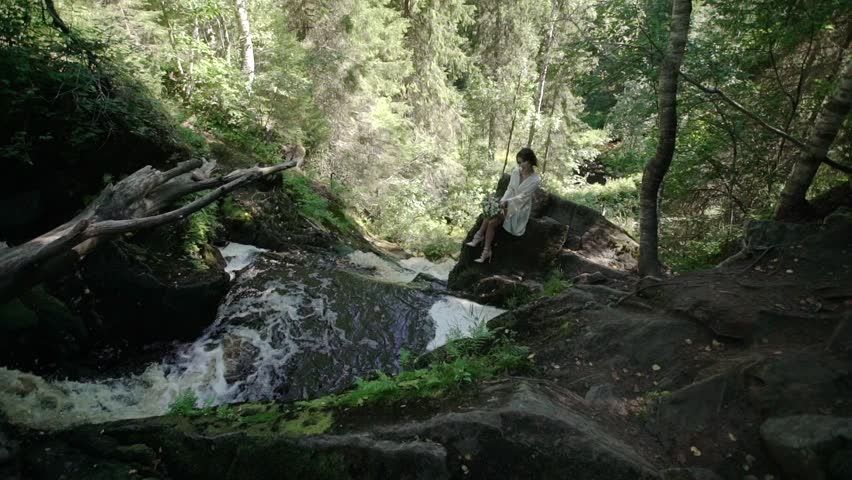 Young woman sitting on a rock near waterfall in lingerie