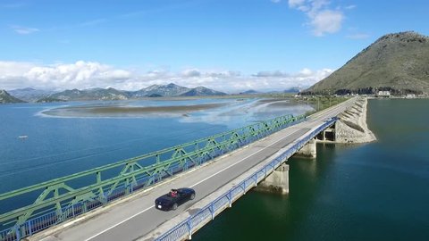 Car drive on beautiful ocean road. Footage. Black car driving on bridge blue sea, mountains and sky background. Car driving near with motion blur showing rapid movement on a highway road at Lake.