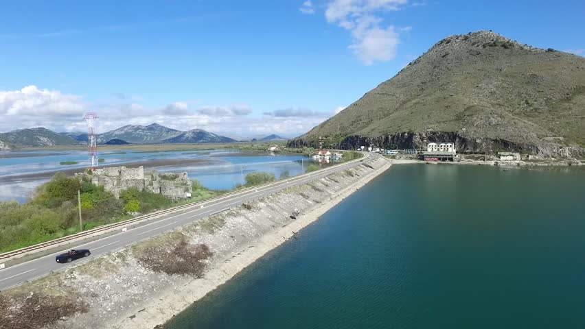 Black car driving on bridge blue sea, mountains and sky background. Footage. Car going on a road near the river, aerial view. Footage. Aerial view at small forest lake and line of highway passing near