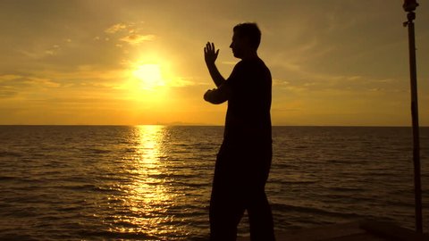 Man is meditates in tai chi style alone. Tai Chi training. Silhouette of a man on the background at sunset of the sea practicing Tai Chi.