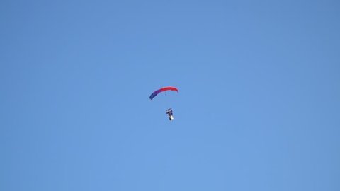 A man on a multi-colored sports parachute with the flag of Ukraine behind him lands in the field