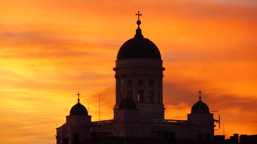 Black silhouetted Helsinki Cathedral domes against outstanding vivid orange clouds over evening sky, telephoto shot. Famous building shadow figure, saturated and rich colored afterglow at clouds