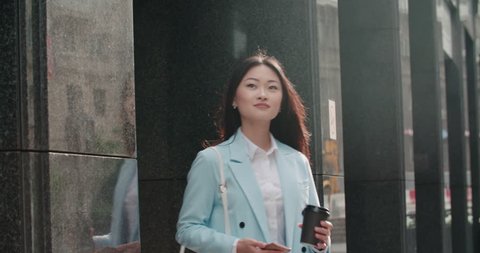beautiful young business Asian woman in a good mood in the morning, goes to work with smartphone and coffee to go, slow motion