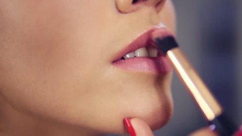 Closeup view of a professional makeup artist applying lipstick on model's lips working in beauty fashion industry. Closeup view of an artist's hand using special brush