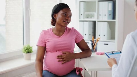 pregnancy, medicine, healthcare and people concept - gynecologist doctor with clipboard and happy pregnant african american woman talking at hospital