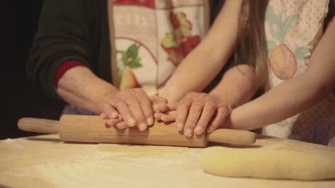 Gorgeous vintage slow motion of an elderly woman a young girl preparing pasta or pizza together using a rolling pin on a sheet of kneading.