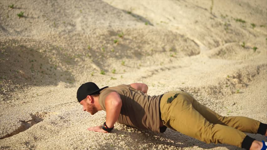 A man does push-ups from the ground and raises his hand to increase the load, an athlete does exercises in nature on a summer day