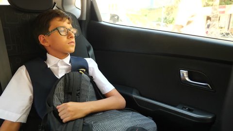 the sad boy is riding in the car in school uniform. 4k, slow-motion
