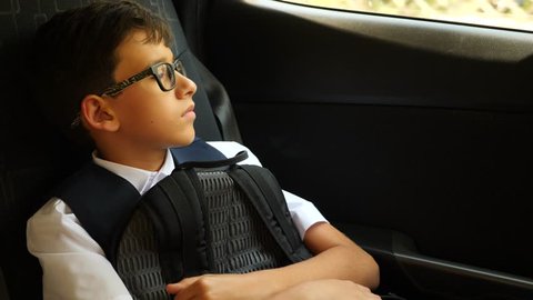 the sad boy is riding in the car in school uniform. 4k, slow-motion