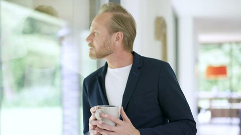 Portrait smiling man in modern home, drinking coffee next to window