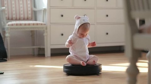 Little baby girl rolling on moving robot vacuum cleaner while cleaning home