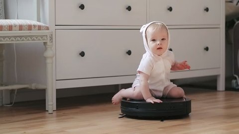 Funny baby girl sitting on spinning robot vacuum cleaner while cleaning room