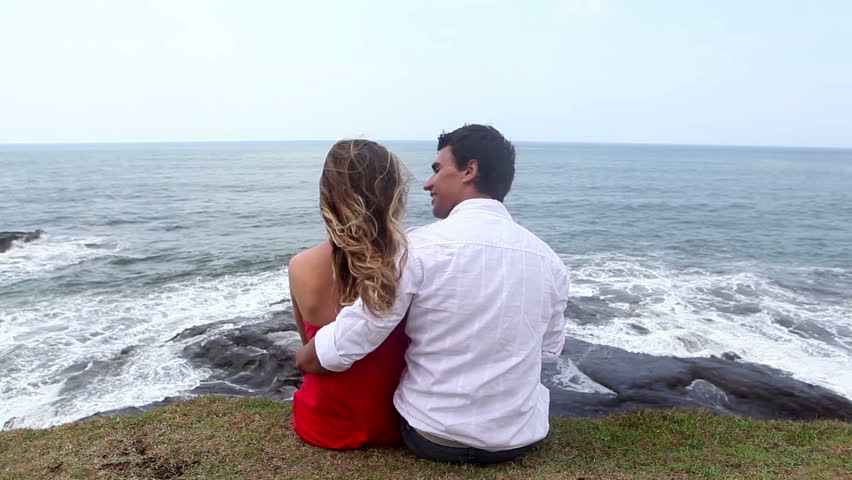 Rear view of couple sitting at coast and looking at ocean