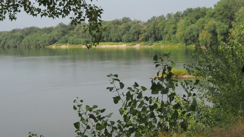A girl with a backpack warms her face in the sun. A girl walks along the river bank.