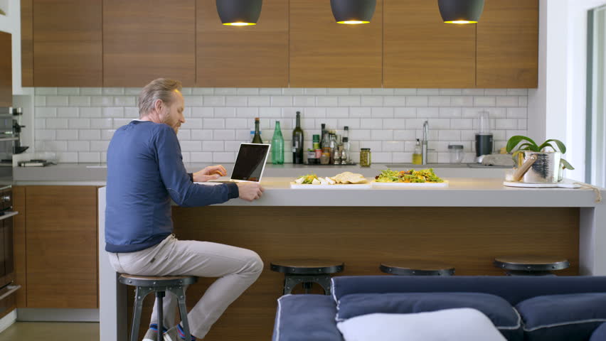 Cheerful couple chatting in the kitchen of modern home, man shopping online