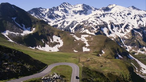 Wide aerial shot of car driving on curving mountain pass / Grossglockner, Austria