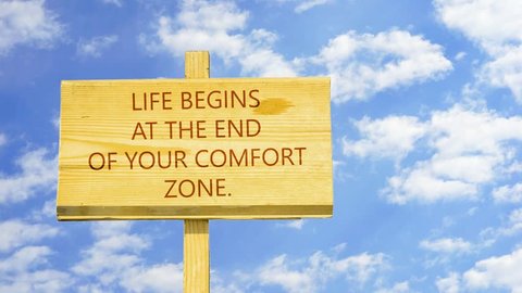Motivational quote to create future. Life begins at the end of your comfort zone. Words on a wooden sign against time lapse clouds in the blue sky.