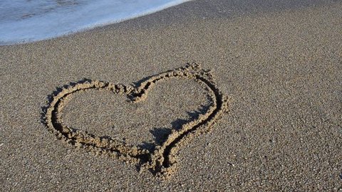 The drawing heart on sand. Heart is washed away by a sea wave.	Shooting on the beach.