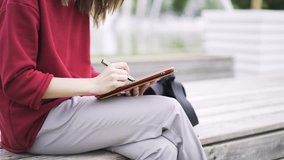 Close up of hands of an unrecognizable young woman wearing a red sweater drawing at her tablet computer with a special pen. Locked down real time close up shot