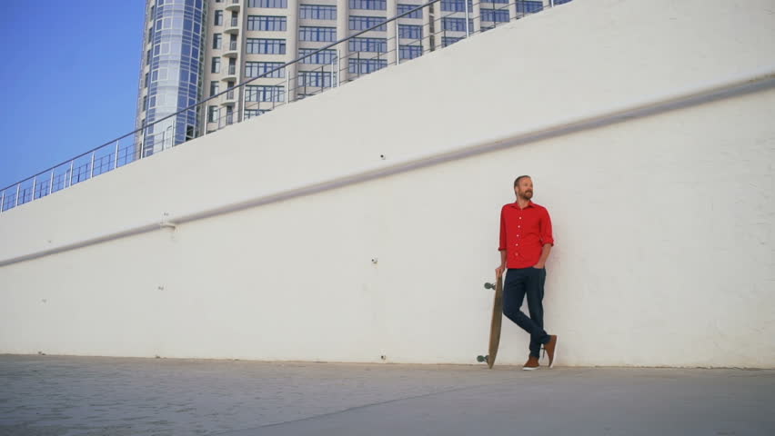 Hipster boy standing with his skateboard in red shirt rapid slow motion 
