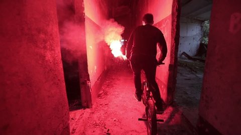 bicyclist with a red signal light in his hand rides over an abandoned building