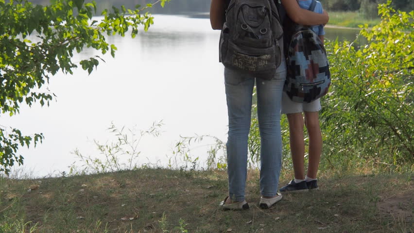 Mom and child are looking at the current river. A woman with a little girl embraced standing on the river bank.
