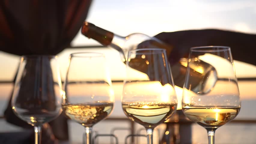 A party by the sea at sunset, pour wine into four glass glasses. HD, 1920x1080. slow motion