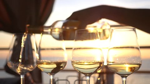 A party by the sea at sunset, pour wine into four glass glasses. HD, 1920x1080. slow motion