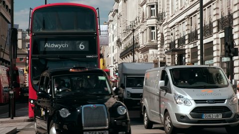 LONDON/UNITED KINGDOM - 11TH AUGUST 2017: Close shot of red London bus and black taxis pass through traffic lights at Piccadilly Circus in London