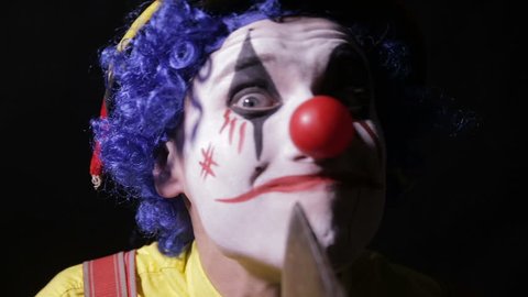 A clown makes face cutting movements with an axe. 