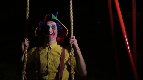 A clown with bloody makeup on swings. 