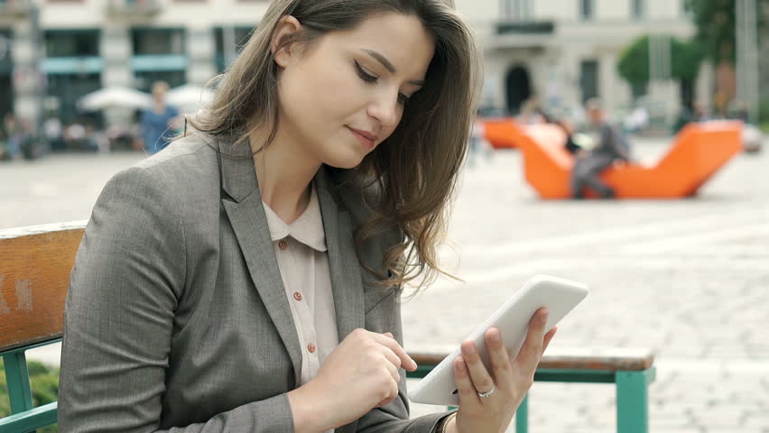 Attractive businesswoman using tablet in the city and smiling to the camera, steadycam shot
