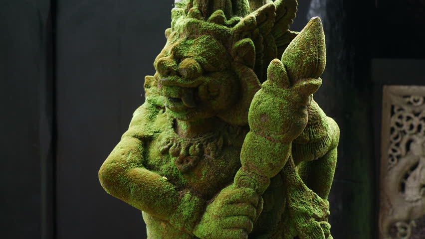 Balinese Carved Stone Statue of Rakasa covered with green moss. at Hindu Temple.