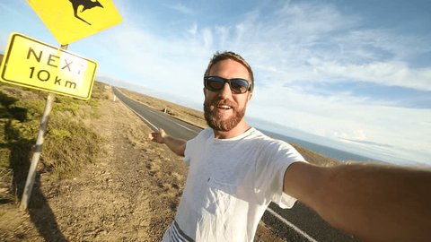 Cheering young man takes selfie portrait next to kangaroo sign.
Cheering young man takes a selfie portrait on the road standing next to a kangaroo warning sign, Australia. Selfie time 
