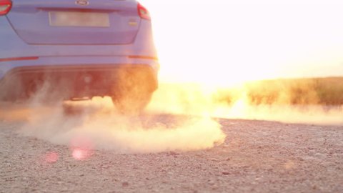 SLOW MOTION CLOSE UP: Sports car starts & quickly drives away from a dusty macadam dirt road raising sand, rocks and stones at dawn. Sportive auto performing burnout at beautiful golden summer sunrise