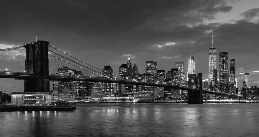 Time-lapse of Lower Manhattan Financial District skyscrapers, Brooklyn Bridge, and East River with passing clouds at twilight in Black  White. Manhattan, New York City